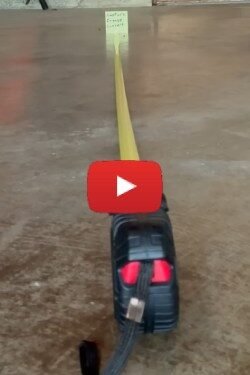 Yellow retractable measuring tape extended along a concrete floor, with the casing visible at foreground and the tape running toward a small label at the far end.